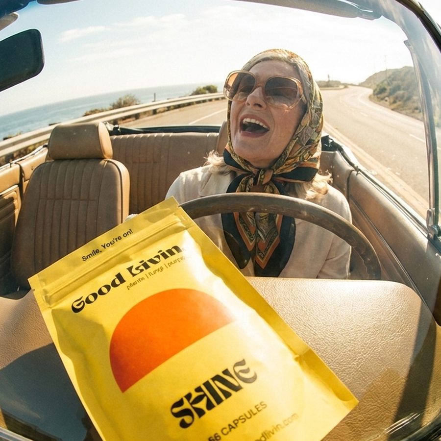 Fisheye shot of a woman in a headscarf laughing behind the wheel of a convertible, a bag of Shine on the dashboard